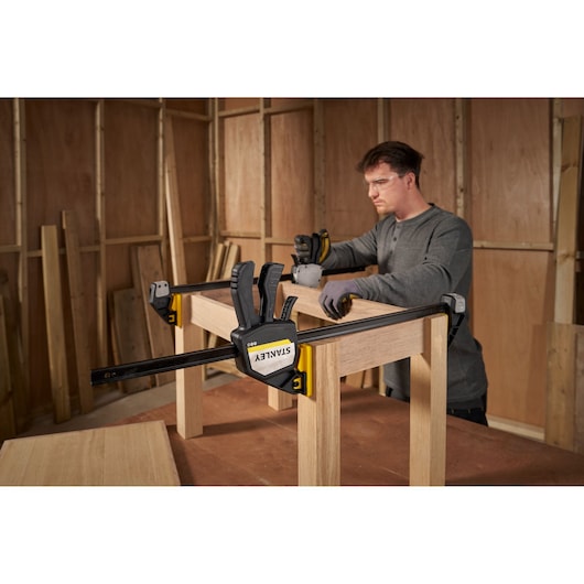 Photo of STANLEY FMHT83281-0 bar clamp securing wooden frame during assembly in workshop setting.