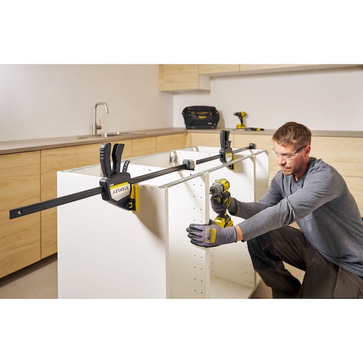 Photo of STANLEY FMHT83281-0 bar clamp securing white cabinet in kitchen assembly scene.