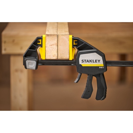 STANLEY FMHT83281-0 trigger clamp securing two wooden boards on a workbench, close-up side view.