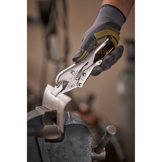 Gloved hand uses STANLEY locking pliers to grip metal piece held in a vise in a workshop setting.