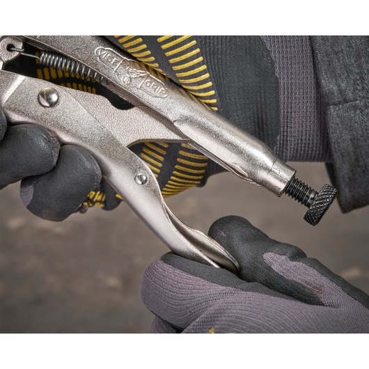 Gloved hand adjusts a metal locking plier tool, close-up view of the handle and adjustment screw.