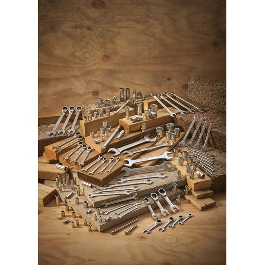 Assorted wrenches and socket tools arranged on wooden blocks and concrete against a wooden background.