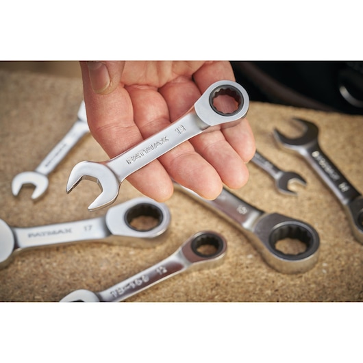 STANLEY FMMT13115-0 ratcheting combination wrench held in hand with other wrenches on a work surface.