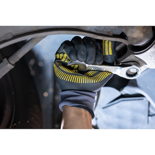 STANLEY FMMT13115-0 ratchet spanner in gloved hand tightening bolt on car part, close-up action photo.