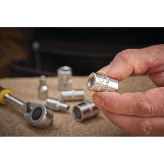 Photo of a hand holding a STANLEY FMMT17193-0 socket with other sockets and a ratchet wrench on a work surface.