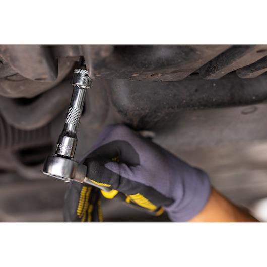 STANLEY FMMT82677-0 ratchet wrench in use under a vehicle, close-up with gloved hand.