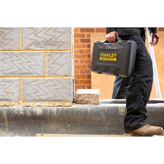 Photo of STANLEY FMMT82683-0 tool case in worker’s hand at construction site, with brick background.