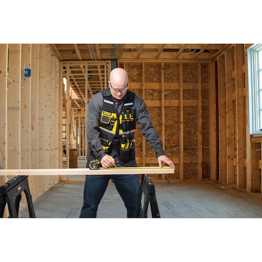 STANLEY FMST1-71181 tool vest with multiple yellow and black pockets, worn by a person working in a wood construction site.