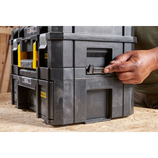STANLEY FMST1-71968 black stackable toolbox with yellow handles, photography showing latch being opened by hand.