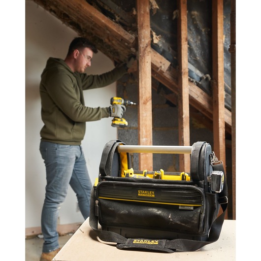 STANLEY FMST17626-1 tool bag with yellow accents on tabletop, person working in background.