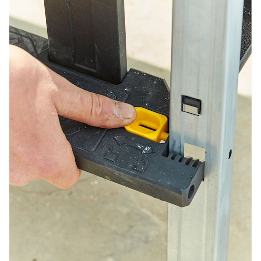 STANLEY FMST81083-1 workbench close-up, hand pressing yellow locking button on black plastic support.