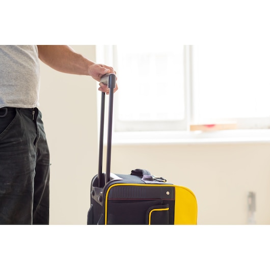 Photo of STANLEY FMST82706-1 black and yellow rolling tool bag, side angle, hand holding telescopic handle.