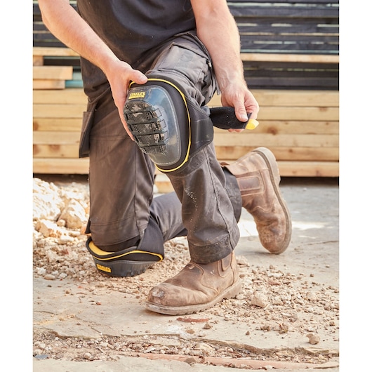 STANLEY FMST82960-1 knee pad with black and yellow trim being strapped on by worker outdoors.