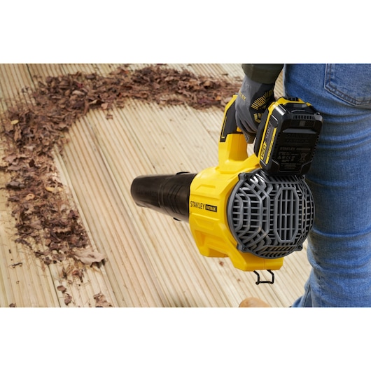 Photo of STANLEY SFMCBL730M1 cordless leaf blower clearing leaves from wooden deck, handheld close-up.