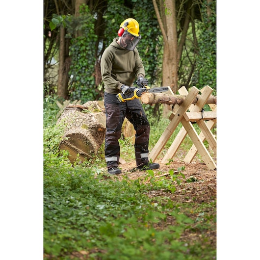 STANLEY SFMCCS730M1 chainsaw in use outdoors cutting wood, shown held by a person wearing safety gear.