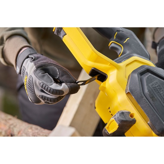 Photo of STANLEY SFMCCS730M1 chainsaw close-up, gloved hand using the tool-less chain tensioner.