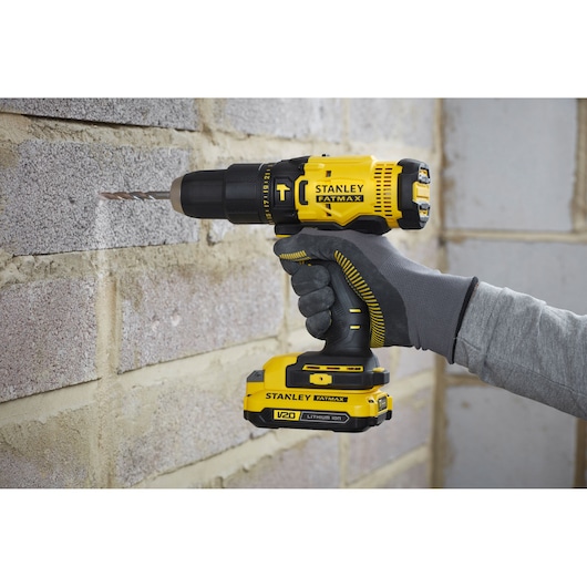 STANLEY SFMCD711C2K cordless drill in use, yellow and black, drilling into masonry wall.