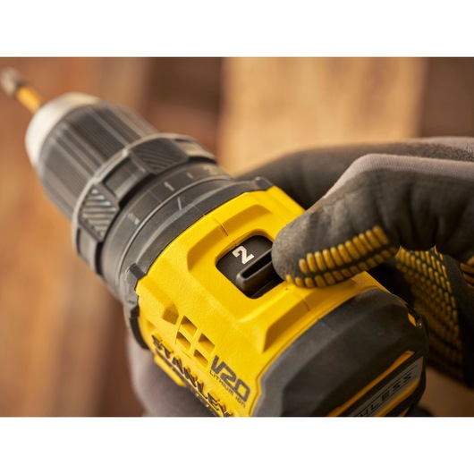 Photo of STANLEY SFMCD714D2T drill close-up, gloved hand adjusting speed setting, yellow and black body.