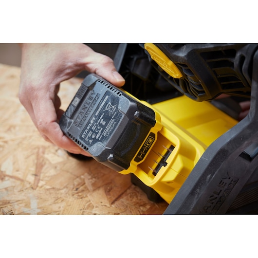 Photo of STANLEY SFMCE001B battery being inserted into a yellow power tool on a wood surface.
