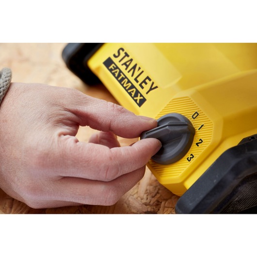 Photo of a hand adjusting the dial on a yellow STANLEY FATMAX SFMCE001B power tool, close-up view.