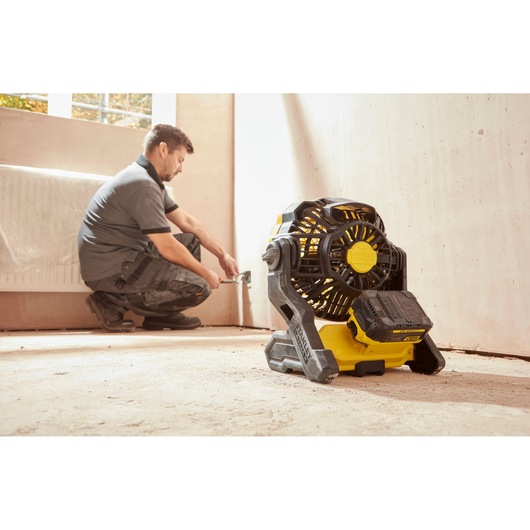 Photo of STANLEY SFMCE001B portable cordless fan in a room with a worker near the wall.