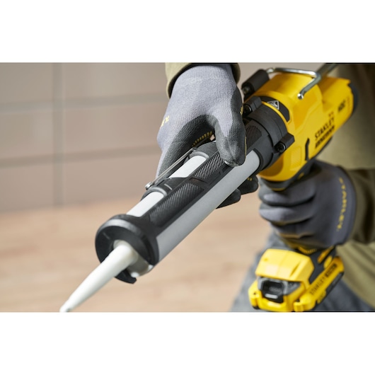 Stanley SFMCE600B cordless caulking gun held by gloved hand, close-up side angle.