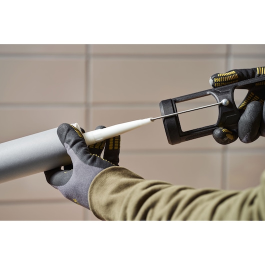 Photo of STANLEY SFMCE600B caulking gun held in gloved hands, applying sealant, side angle.