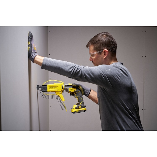 Stanley SFMCF600B cordless screw gun being used by a person to fasten drywall, side view.
