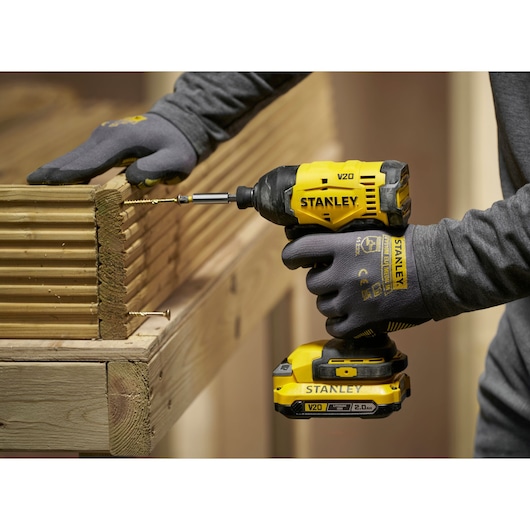 Stanley V20 cordless impact driver drilling screw into wooden boards, person wearing work gloves.