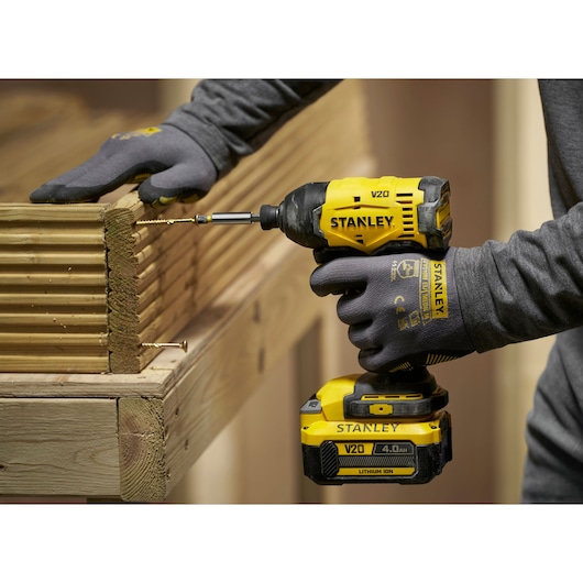 Stanley V20 cordless impact driver used to drill screws into wooden boards in a construction setting.