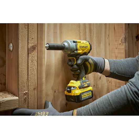 Stanley cordless impact wrench in use on wooden surface, held by gloved hands.