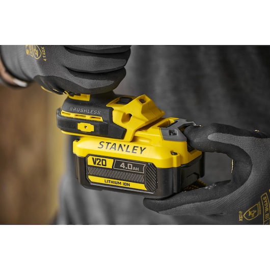 Gloved hands holding a yellow STANLEY V20 4.0Ah lithium-ion battery for power tools.