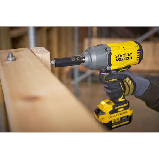 Photo of STANLEY SFMCF940M1 cordless impact wrench being used to fasten a bolt on wooden beams, close-up angle.