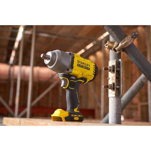 STANLEY SFMCF940M1 cordless impact wrench on construction site, yellow and black body, side view.