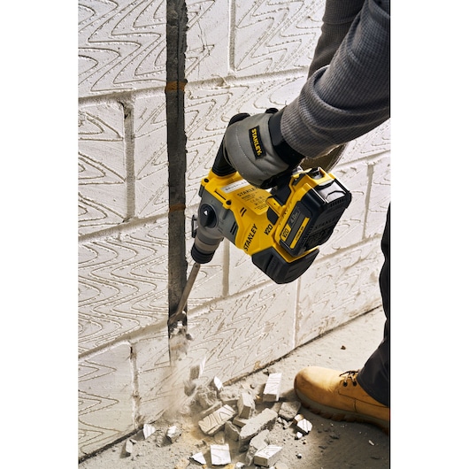 STANLEY SFMCH910B rotary hammer in use chiseling white brick wall, handheld, visible rubble and dust.