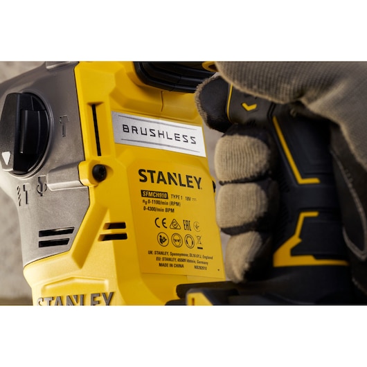 STANLEY SFMCH910B brushless drill close-up held by gloved hand, yellow and black housing, side angle.