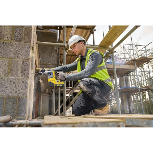 STANLEY SFMCH910M1T rotary hammer drill in use at construction site, worker drilling into brick wall.