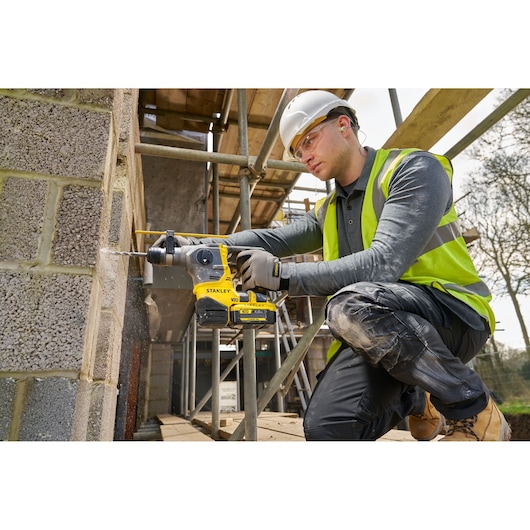 STANLEY SFMCH910M1T rotary hammer drill in use on a construction site drilling into a concrete block wall.