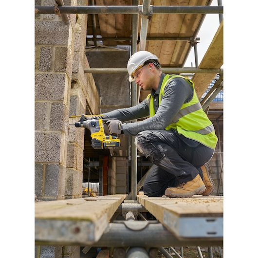 STANLEY SFMCH910M1T rotary hammer drill in use on a construction site, worker drilling into concrete blocks.