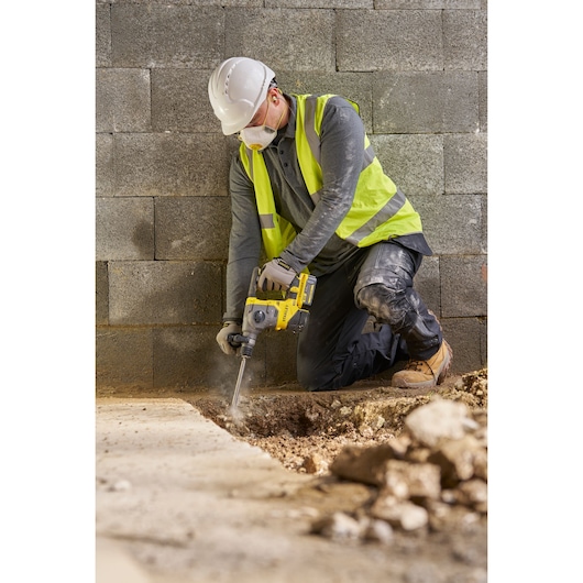 Photo of worker using STANLEY SFMCH910M1T rotary hammer drill at construction site, drilling concrete floor.