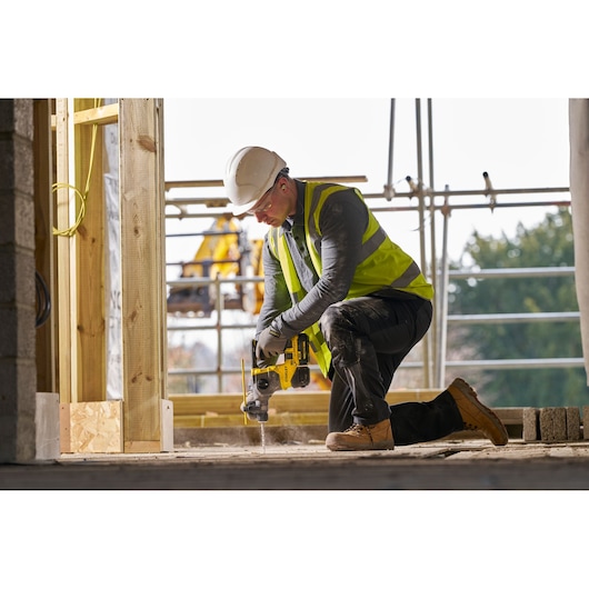 STANLEY SFMCH910M1T rotary hammer drill used by a worker in safety gear on a construction site, side view.