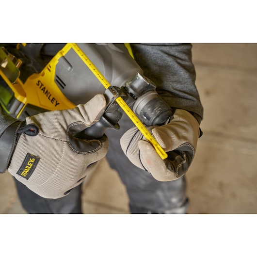 Photo of STANLEY SFMCH910M1T rotary hammer with ruler depth guide, close-up with gloved hands.