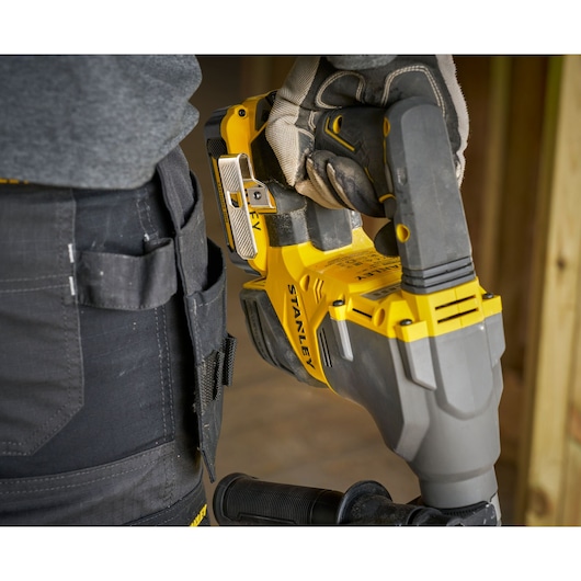 STANLEY SFMCH910M1T rotary hammer held by gloved hand, side view, yellow and gray body, construction setting.