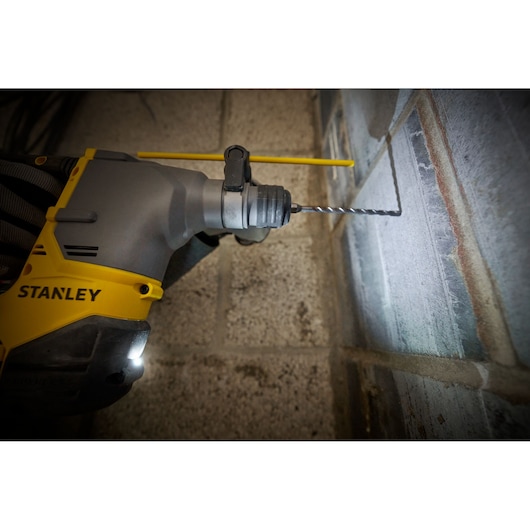 STANLEY SFMCH910M1T rotary hammer drill bit in action drilling into concrete wall, close-up side angle.