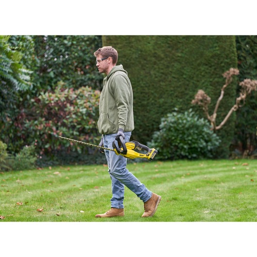 Photo of STANLEY SFMCHT655B hedge trimmer being carried by person in garden.