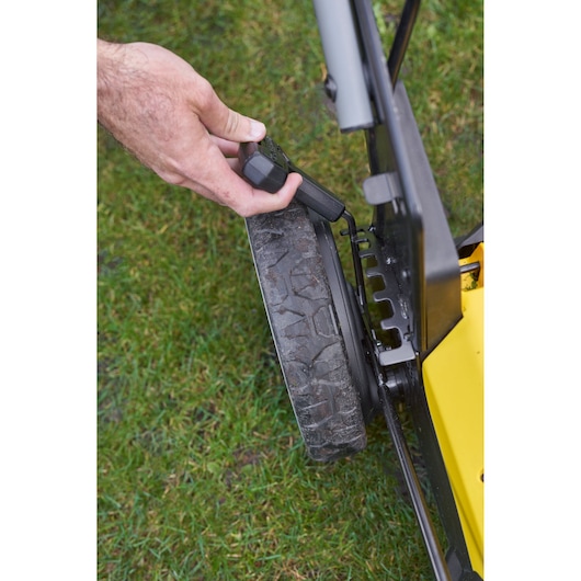 STANLEY SFMCMWS251M lawn mower close-up, hand adjusting wheel height lever, shown on grass.