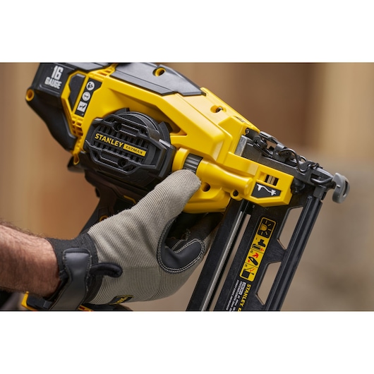 STANLEY SFMCN616B nailer in yellow and black, close-up with gloved hand adjusting tool.