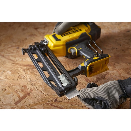 STANLEY SFMCN616B nailer angled view, yellow and black, being loaded with nails on wooden surface.