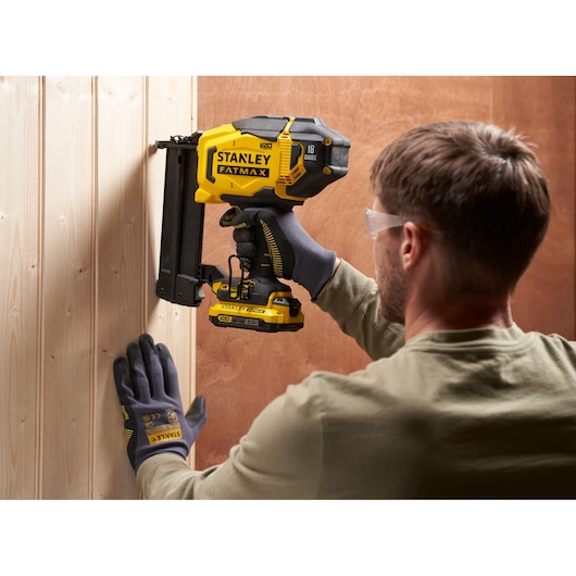 STANLEY SFMCN618B-XJ photography of cordless nailer in use, yellow and black, held against wooden wall.