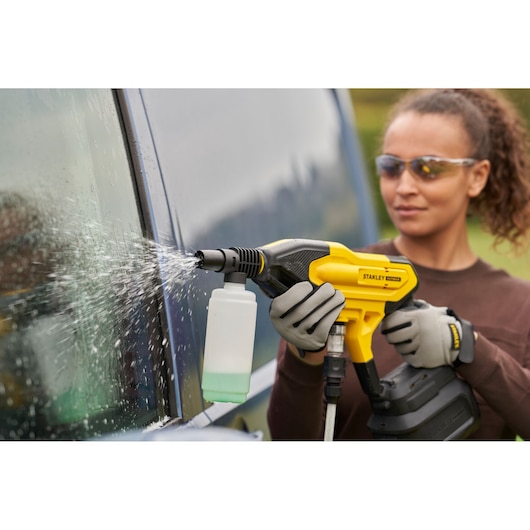 Stanley SFMCPC93B cordless power cleaner spraying water on a car window, close-up, outdoors.